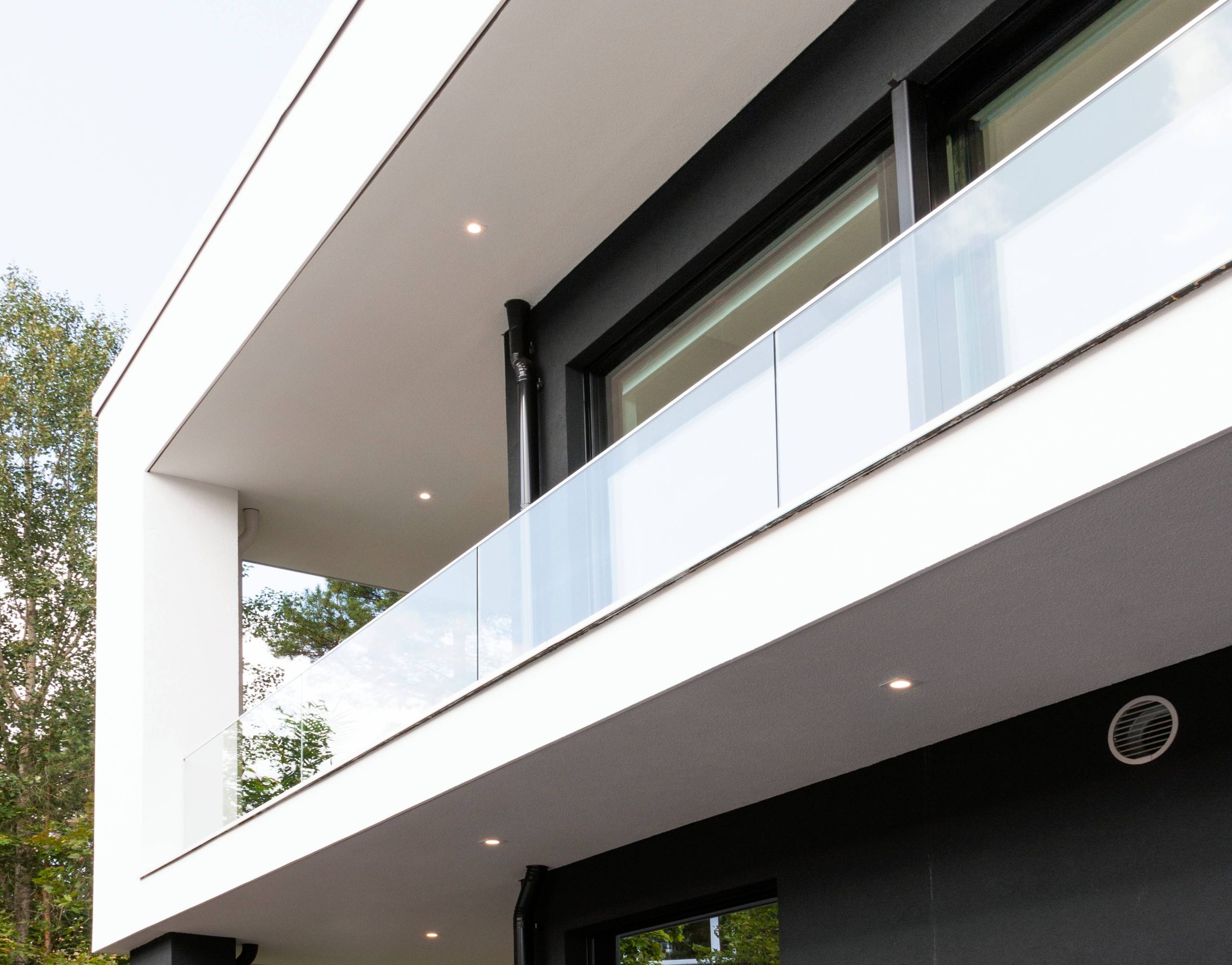 LedStore.fi -verkkokaupassa löydät ihastuttavat LED-valaistusratkaisut, jotka tuovat modernia ilmettä kaksikerroksisen rakennuksen ulkoasuun. Minimalistinen design korostuu suurten ikkunoiden LED-tehosteilla sekä lasisella parvekkeella. Rakenteen tyylikäs sekoitus valkoisia ja tummanharmaita pintoja luo kauniin kontrastin lämpötilalle vehreydelle kirkkaan taivaan alla.