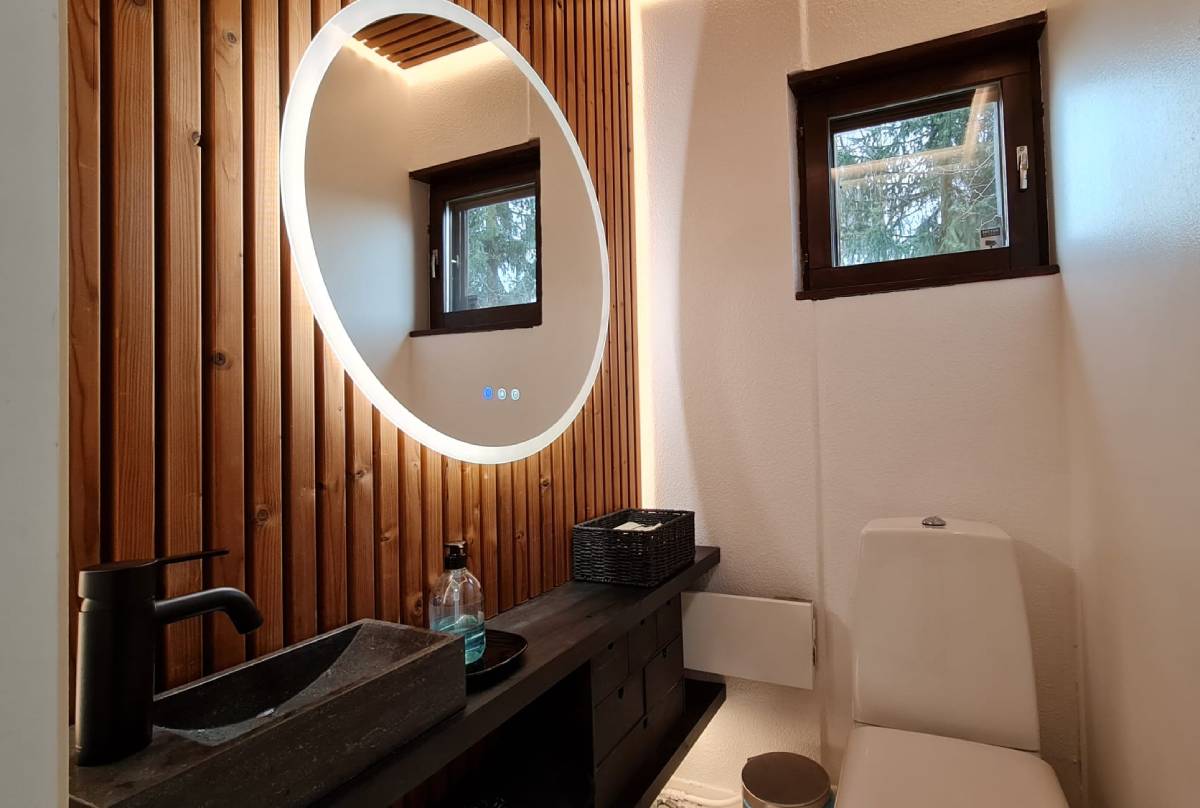 Nykyaikainen kylpyhuone LedStore.fi:n tarjoamalla led-valaistuksella sisältää pyöreän LED-valopeilin, joka on päällä puupaneeliseinälle. Peilin alapuolella on musta työtaso, jossa on suorakulmainen pesuallas ja musta hana sekä saippua-annostelija. WC-istuimen yläpuolella pieni ikkuna, ja lähettyvillä tarjotaan kätevän säilytysratkaisun.